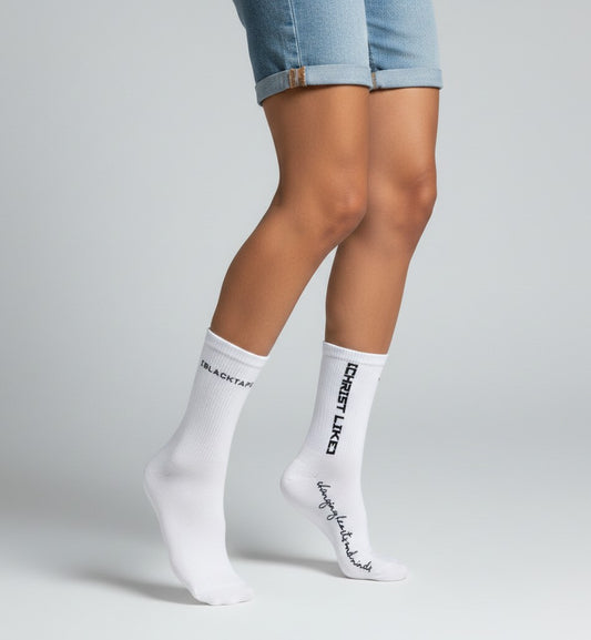 Blacktapechamchristlike white cotton crew socks with black embroidered text worn by a person in denim shorts
